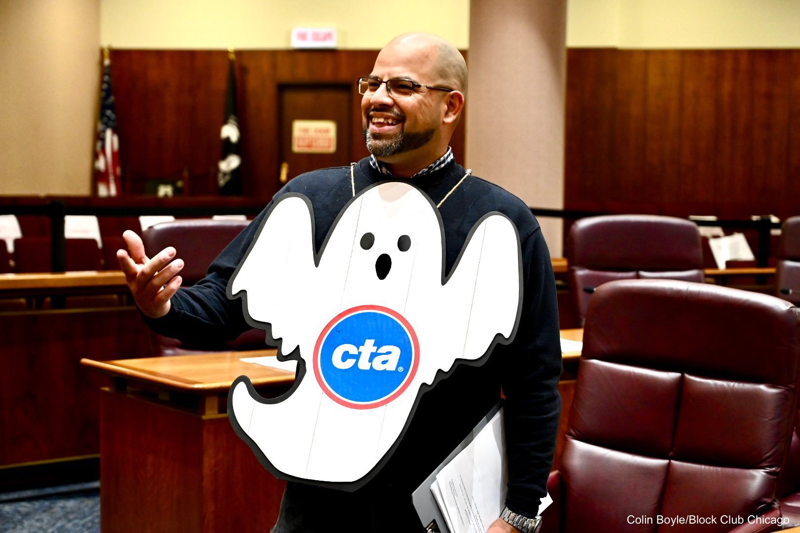 Andre Vasquez smiles at a pre-halloween City Council meeting wearing a "ghost" placard that has the CTA logo on it.